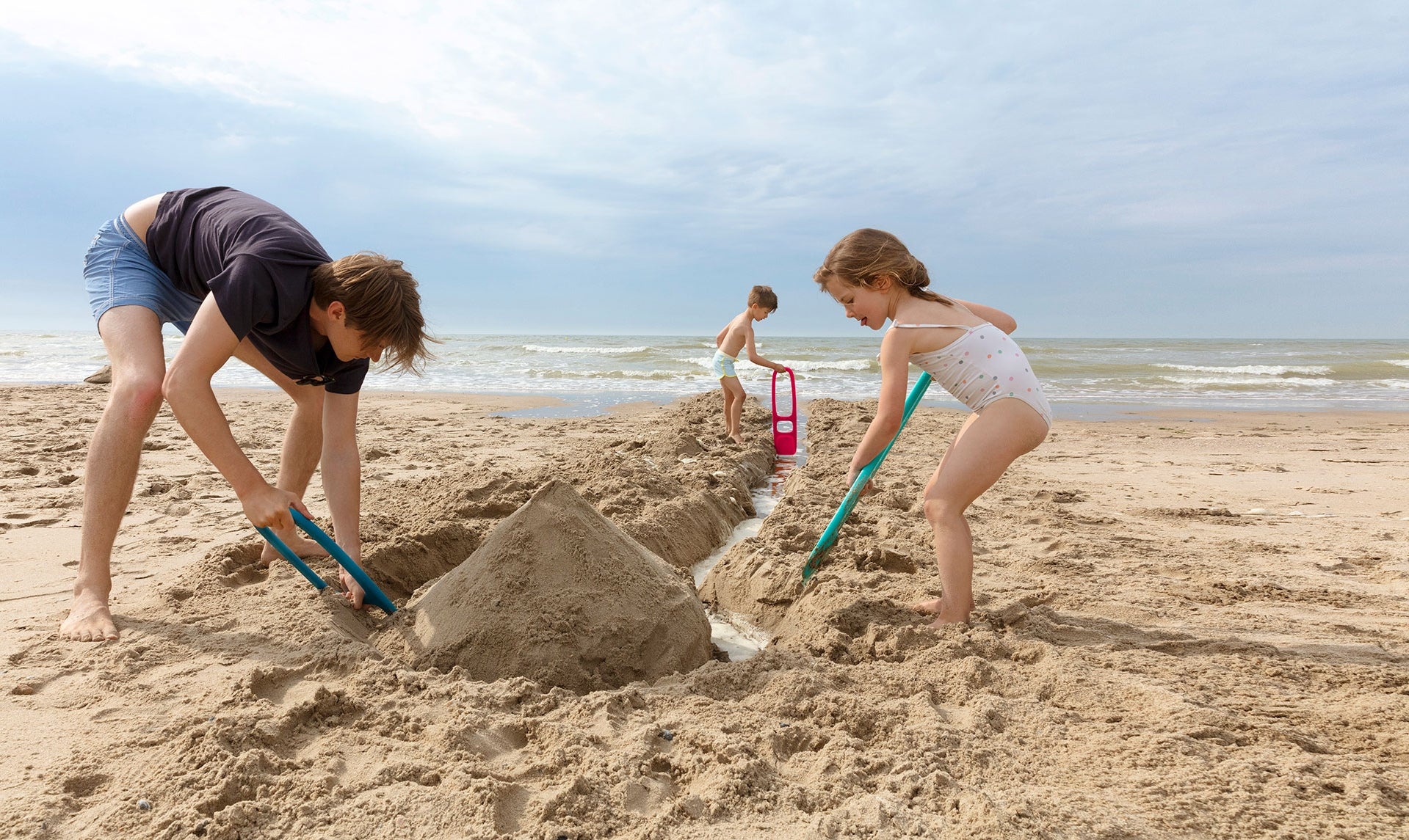 Two children building a sandcastle on a beach with a clear sky.
