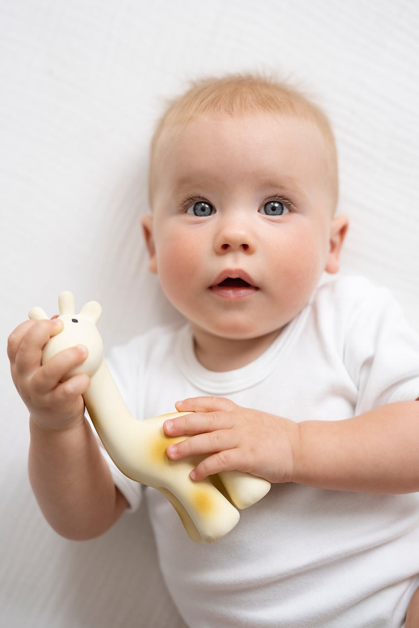 Baby holding a giraffe toy against a white background