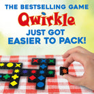 A hand holds a small black game piece with a star symbol over a red-and-white checkered tablecloth, with Qwirkle game boards visible. Large text at the top reads 'THE BESTSELLING GAME Qwirkle JUST GOT EASIER TO PACK!'.