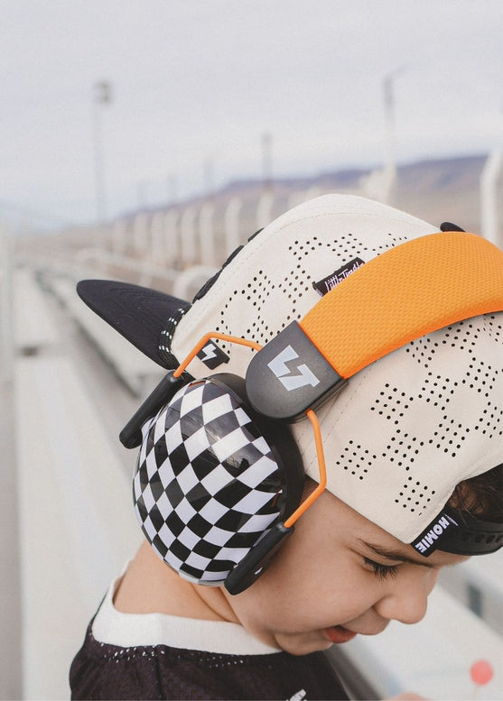 Person wearing a unique helmet with checkered design and orange accents, standing against a blurred background.