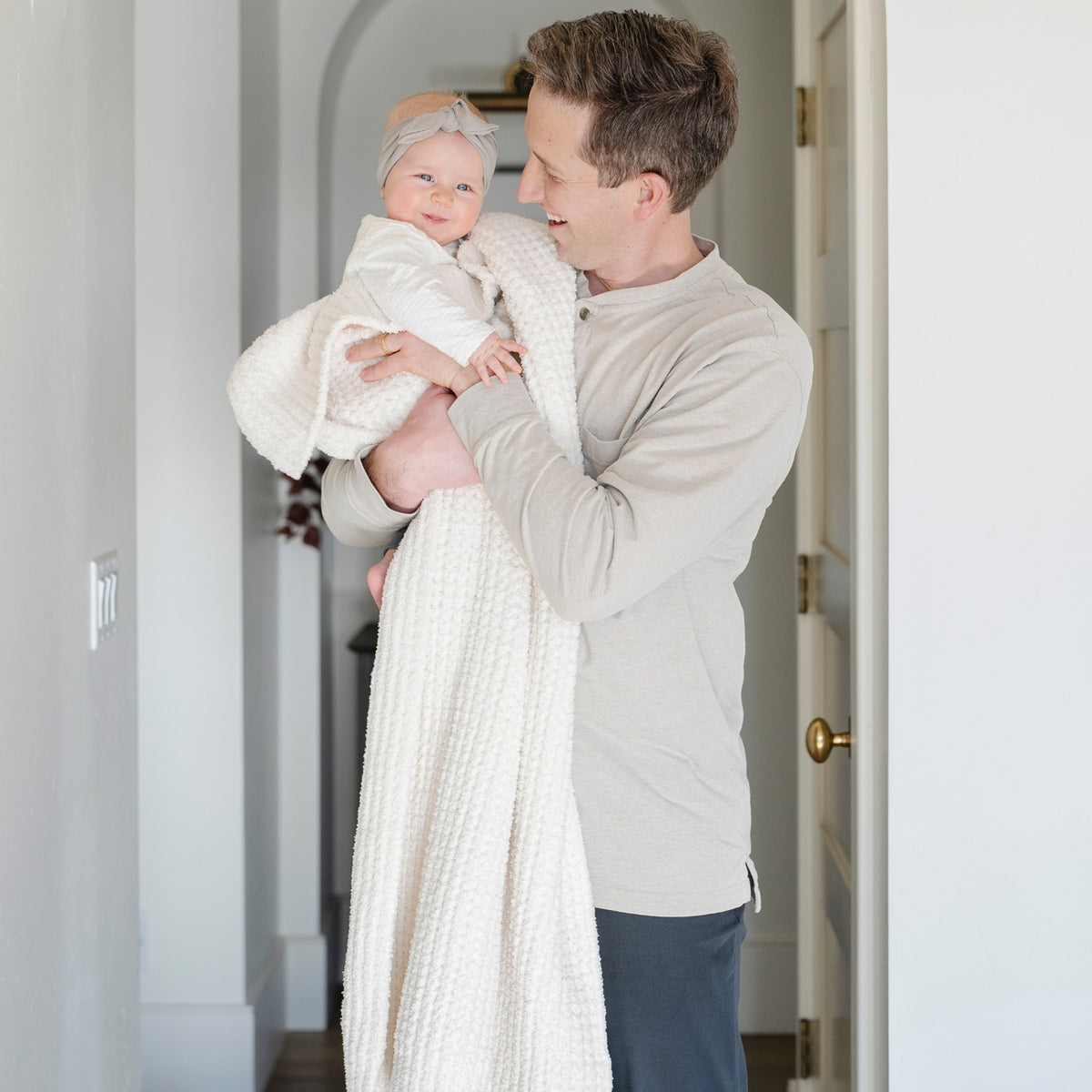 Man holding a baby wrapped in a white blanket in a home setting