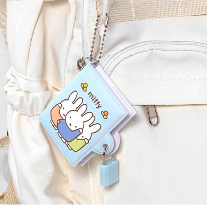 Small blue book-shaped keychain with a cartoon character attached to a white bag.
