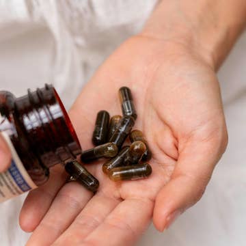 Hand holding capsules with a bottle of supplements in the background