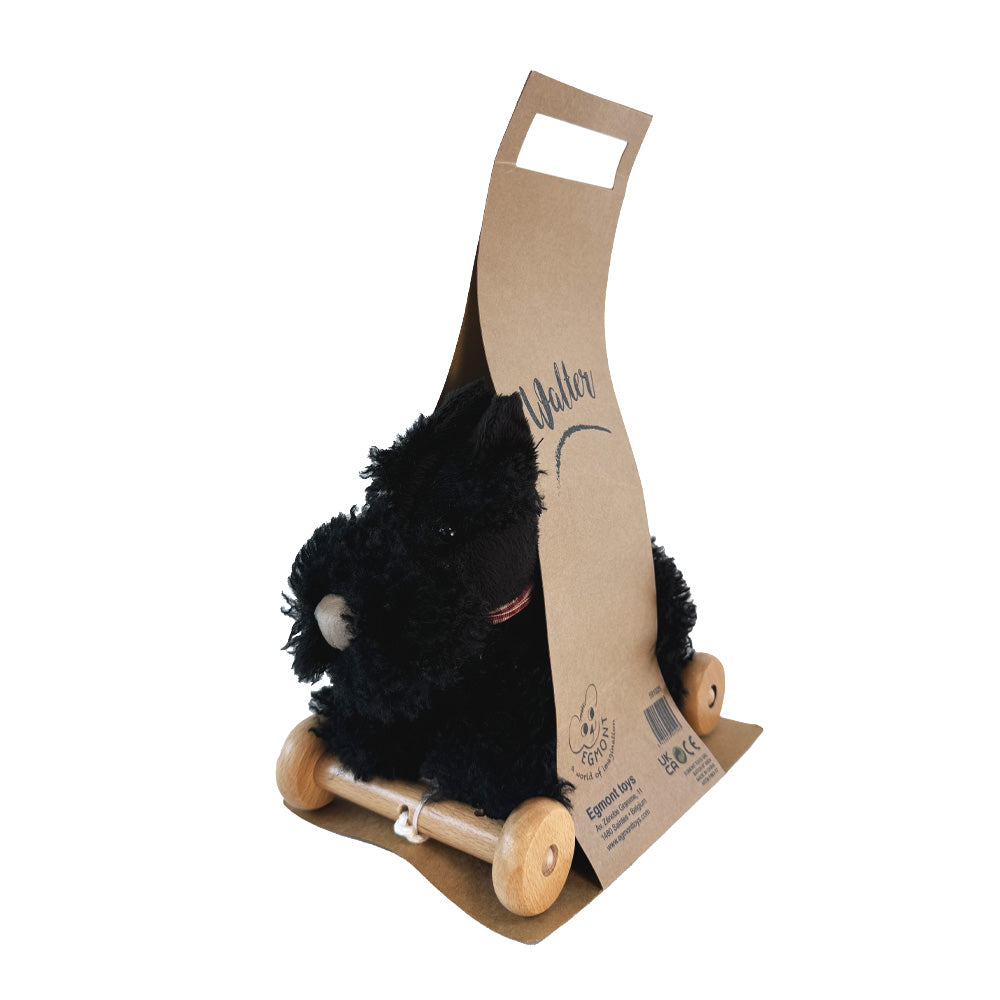 Black plush toy with wooden wheels on a cardboard stand with 'Koller' branding.