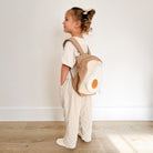 Child wearing a backpack shaped like an egg on a wooden floor.