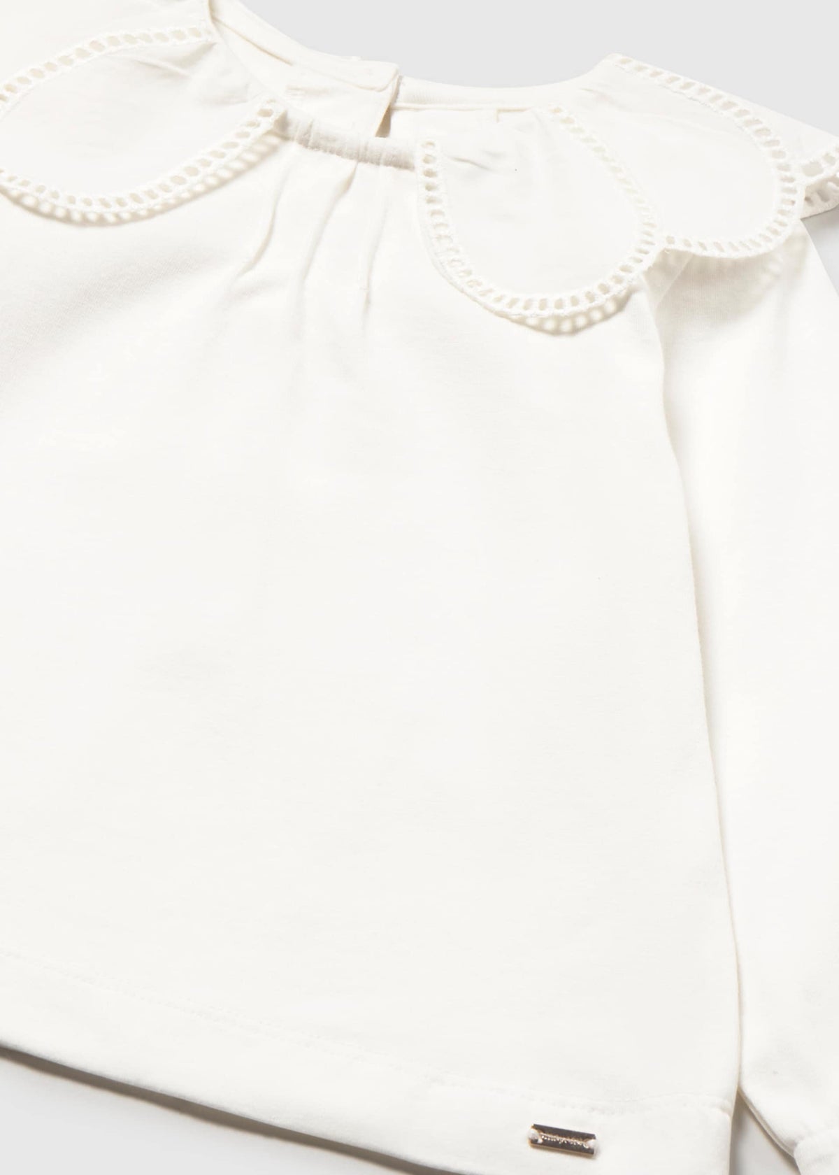 Close-up of a white long-sleeve blouse with a large decorative ruffled collar and a small metallic brand tag near the lower hem.