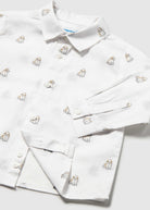 A white long-sleeve button-up shirt with an all-over embroidered pattern of small dogs, shown folded on a light gray background.