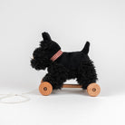 Black dog-shaped pull toy with wooden wheels on a white background