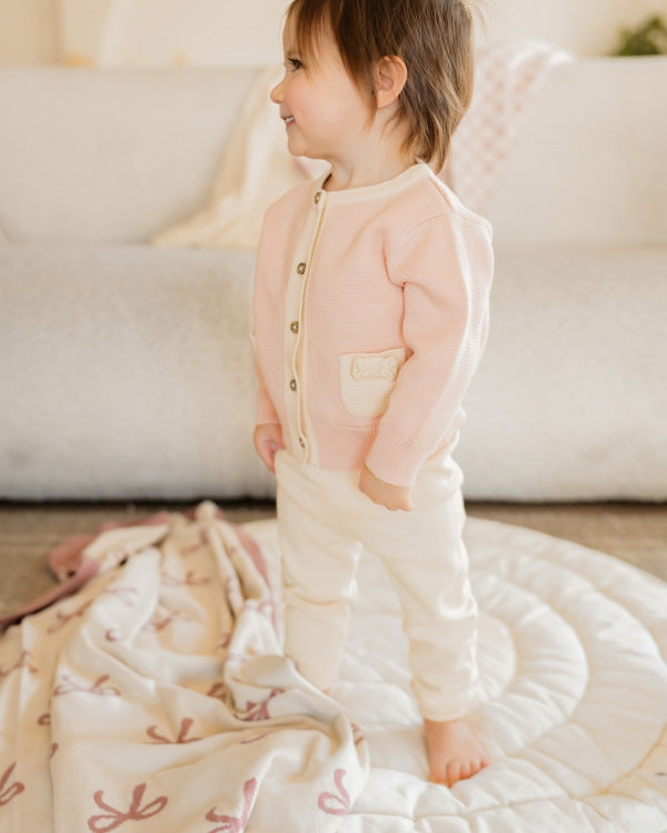 Child wearing a pink outfit with a white blanket and sofa in the background