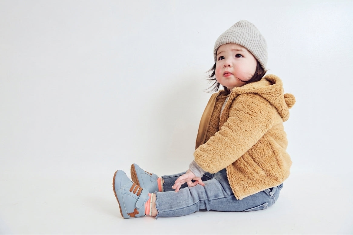 A baby boy wearing brown jacket and  pair of blue baby shoes with brown accents on a white background