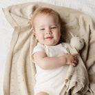 Baby lying on a beige blanket holding a soft toy