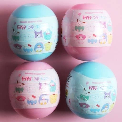 Four colorful spherical toys with cartoon designs on a pink background