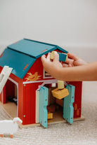 A child’s hands operating the working pulley system on the Wooden Big Red Barn Playset by Mentari, lifting a yellow magnetic hay bale toward the loft while open double doors reveal a glimpse inside the red barn.