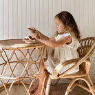 Young girl sitting at a wicker table with a wicker chair, playing with toys.