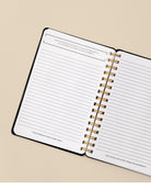Open spiral-bound planner with lined pages on a beige background