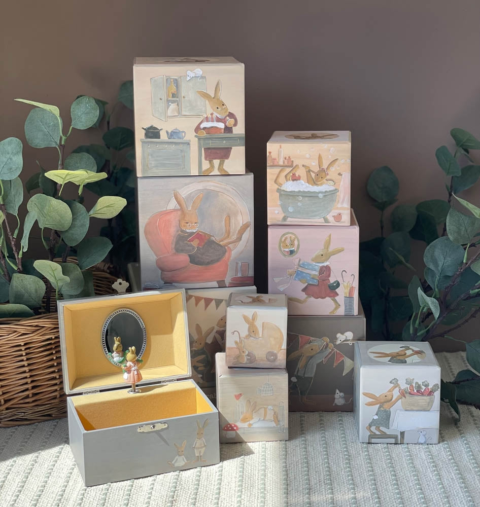 Set of decorative boxes with illustrated scenes and a jewelry box on a surface with plants in the background.