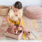 Child playing with dolls in a room with a textured rug and woven baskets.