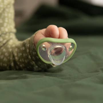 Baby's hand holding a green pacifier on a green blanket