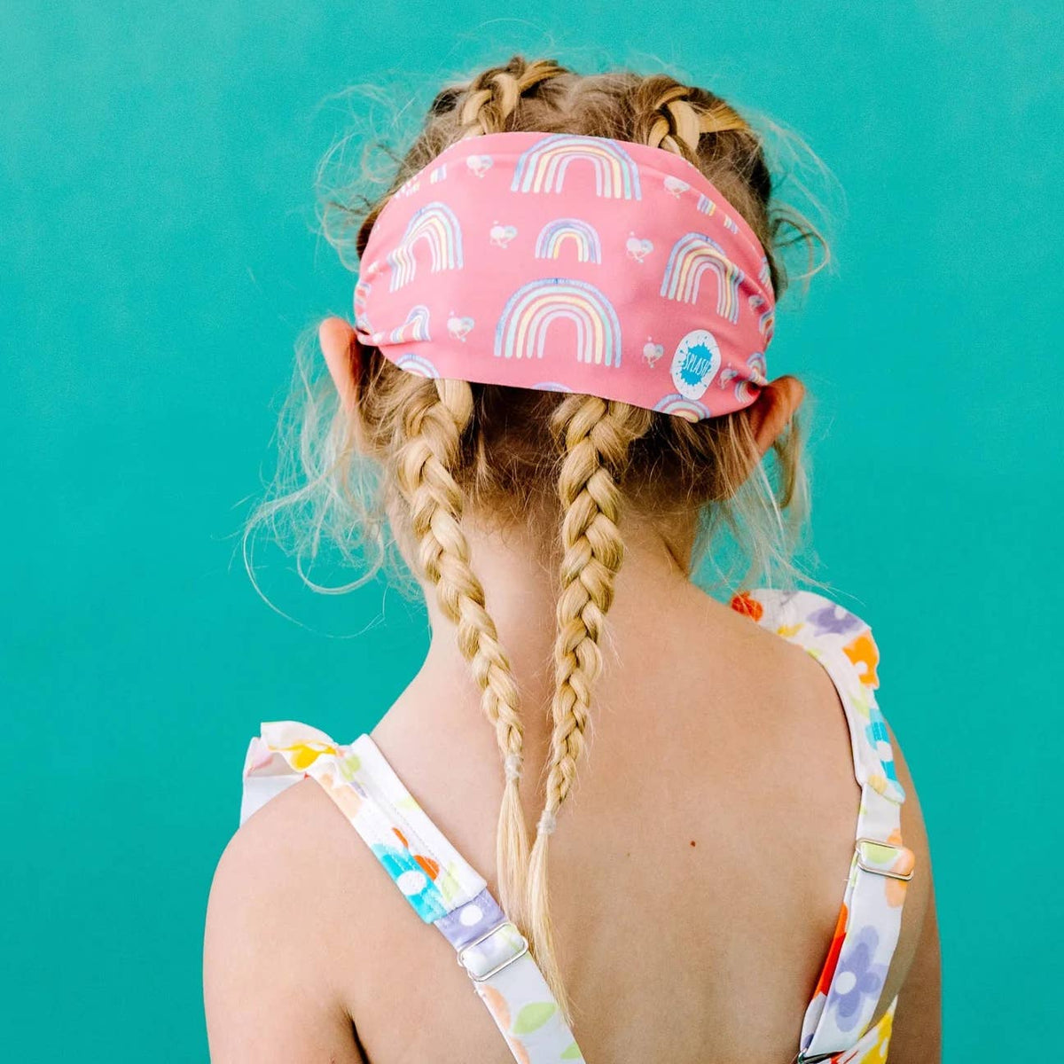 Child wearing a pink headband with rainbow patterns against a teal background