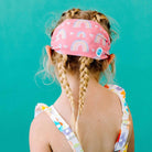Child wearing a pink headband with rainbow patterns against a teal background