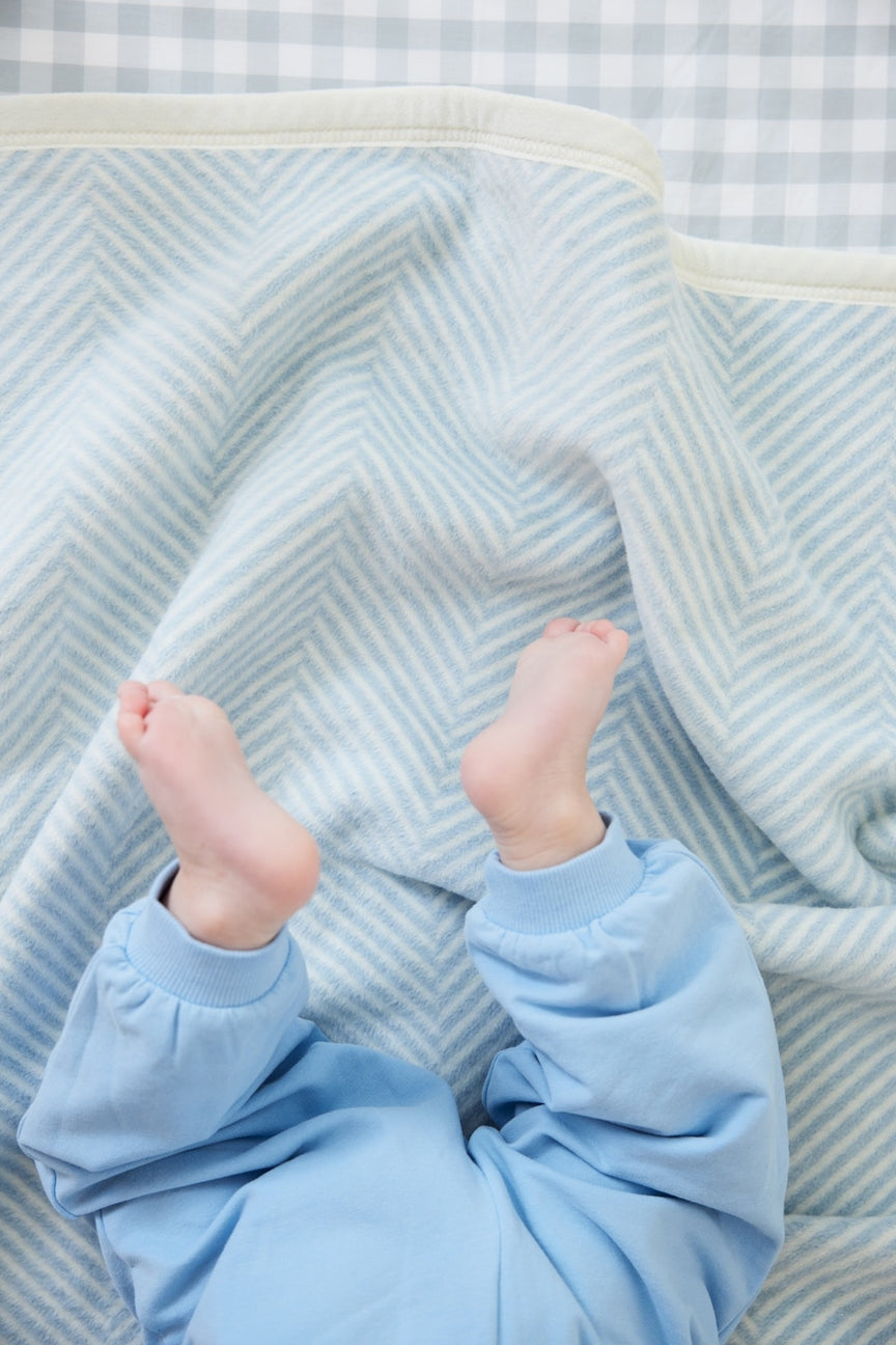 Baby's feet peeking out from under a light blue blanket with a striped background