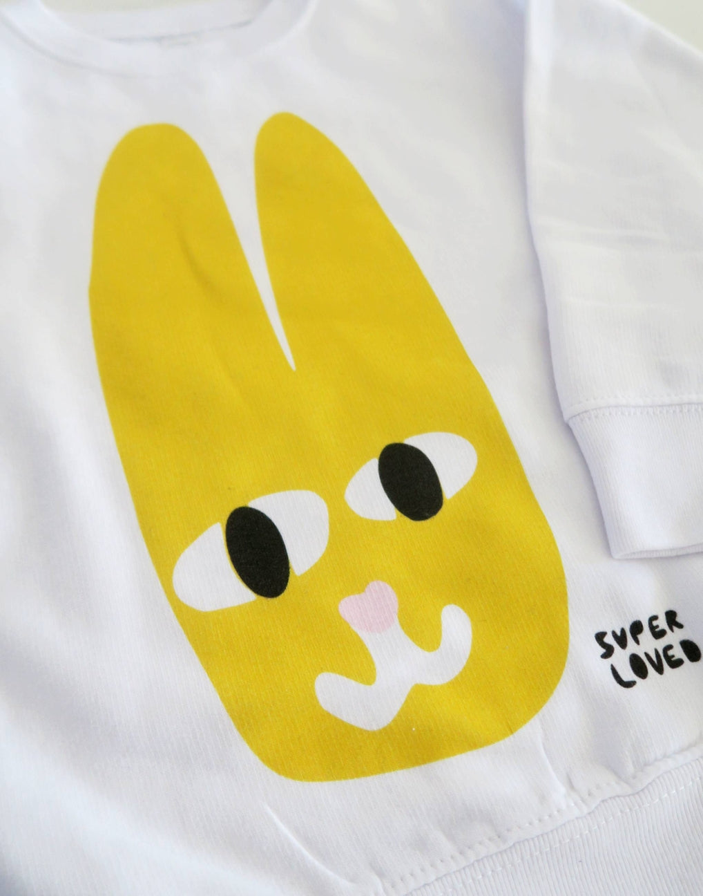 White shirt with a yellow cartoon bunny face and 'SUPER LOVED' text on a white background