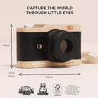 A wooden toy camera with a black faux-leather body and black lens, shown with dimension arrows and text indicating 60mm height, 58mm depth, and 105mm width. The top of the image reads 'CAPTURE THE WORLD THROUGH LITTLE EYES' and the bottom includes sustainability and eco-friendly badges.