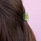 Green hair clip on a person's hair against a pink background