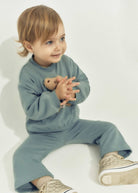 Child wearing a blue outfit holding a teddy bear on a white background