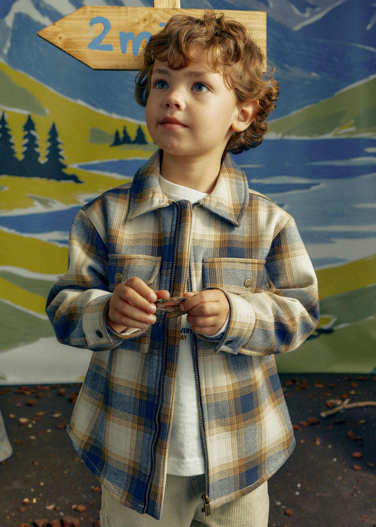Child wearing a plaid shirt with a scenic background