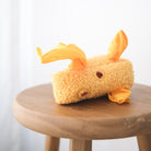 Plush toy resembling a cartoon character on a wooden stool with a white background