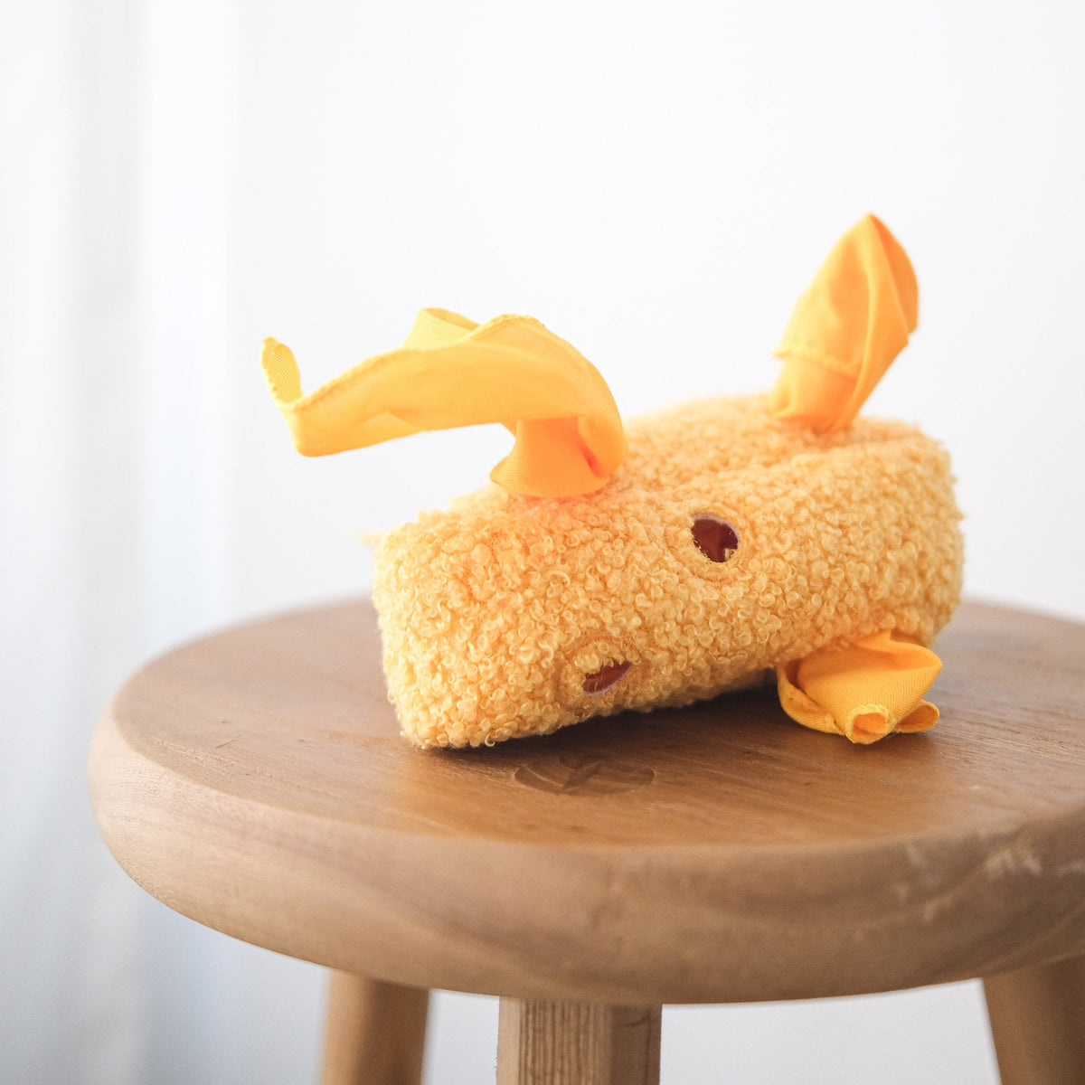 Plush toy resembling a cartoon character on a wooden stool with a white background