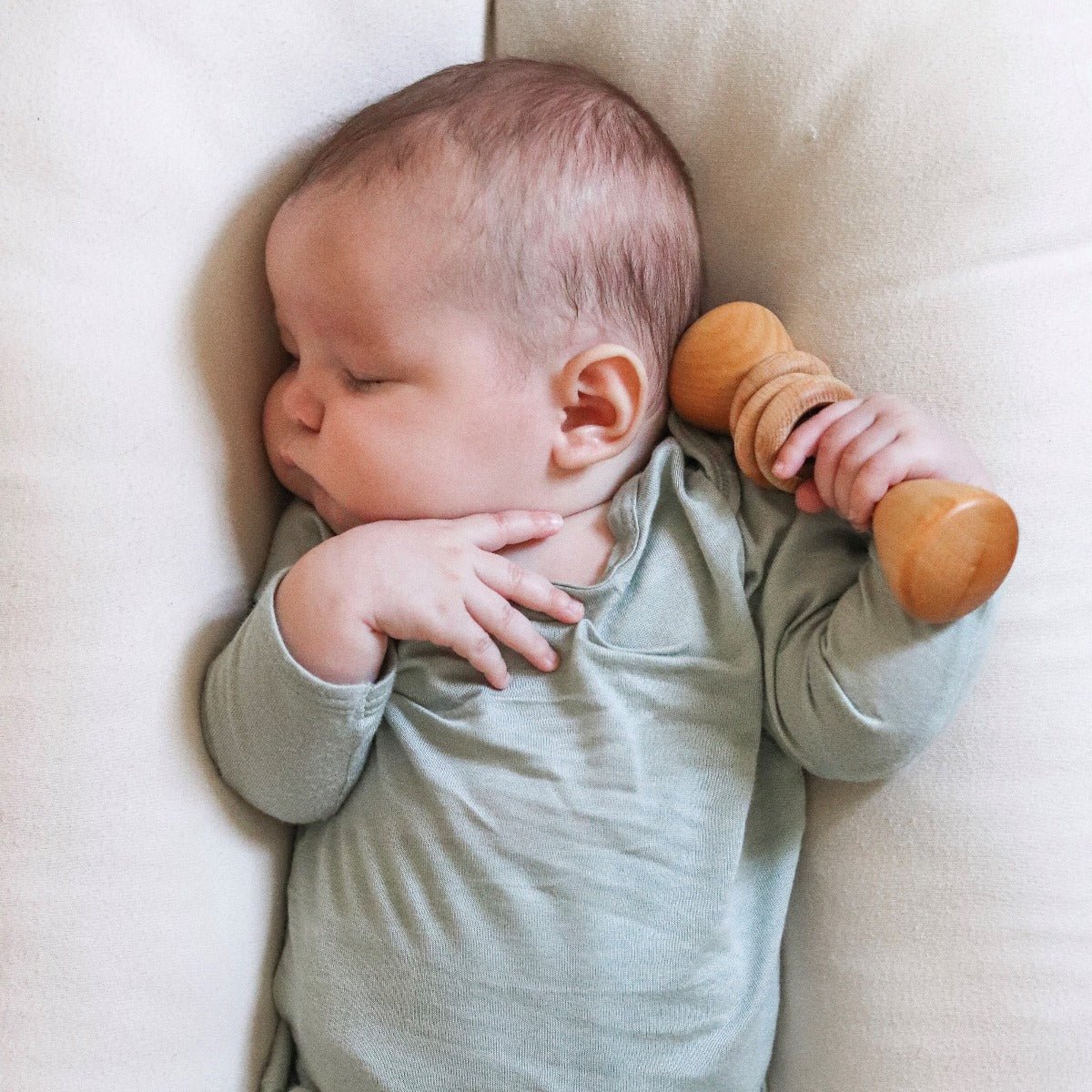 Baby lying on a beige surface holding a wooden toy