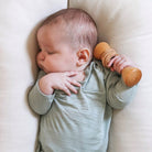 Baby lying on a beige surface holding a wooden toy