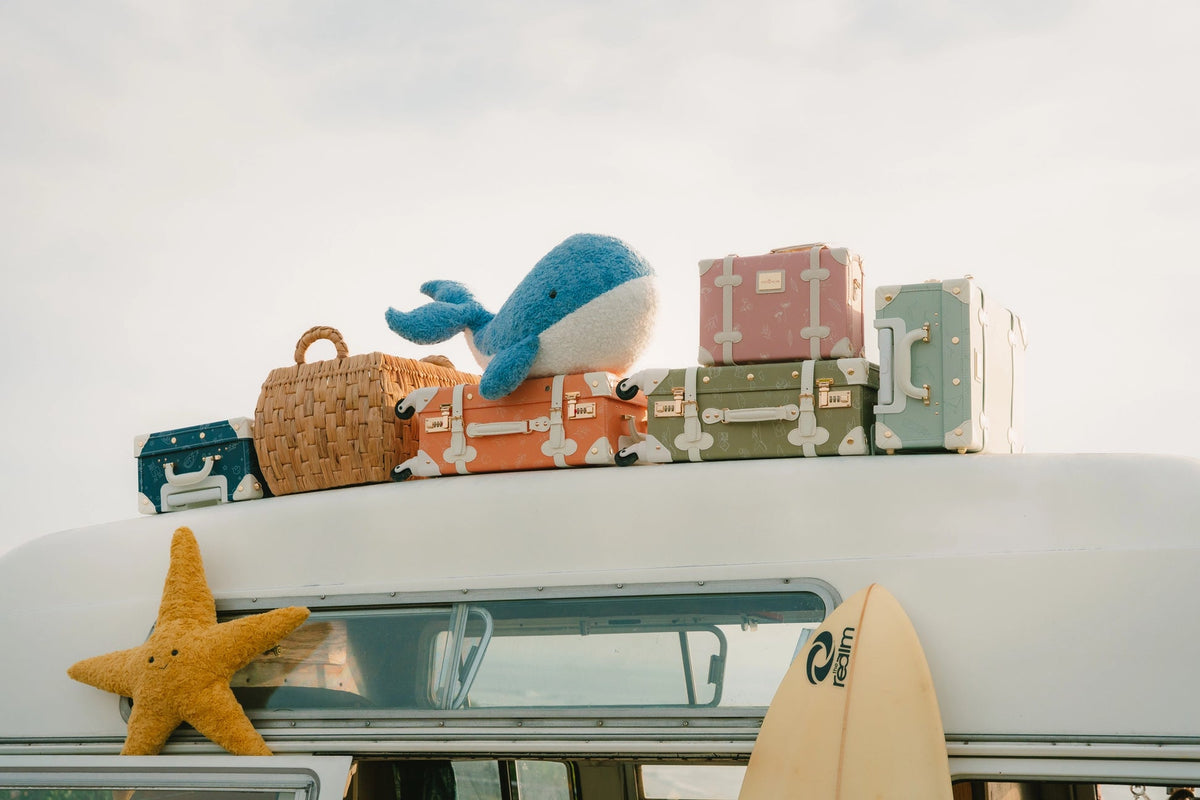 Stack of colorful suitcases with a plush toy on top, next to a surfboard and starfish.