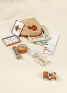 Collection of art supplies including paint tubes, canvases, and a wooden toy on a beige background