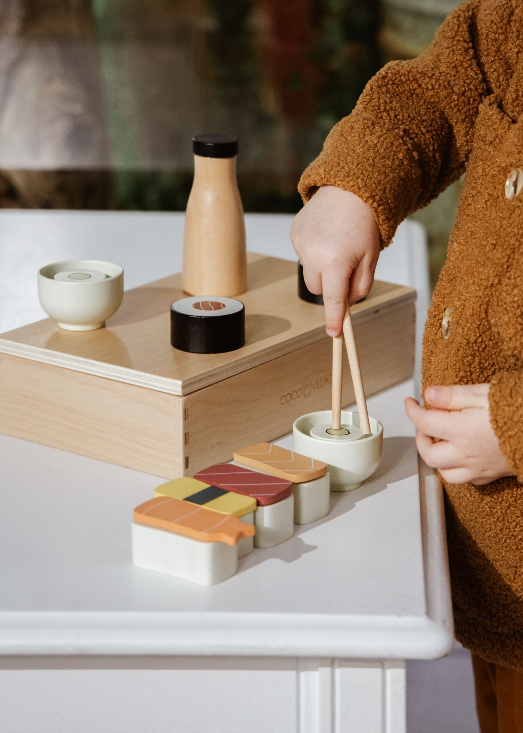 Child playing with wooden toy food set on a white surface