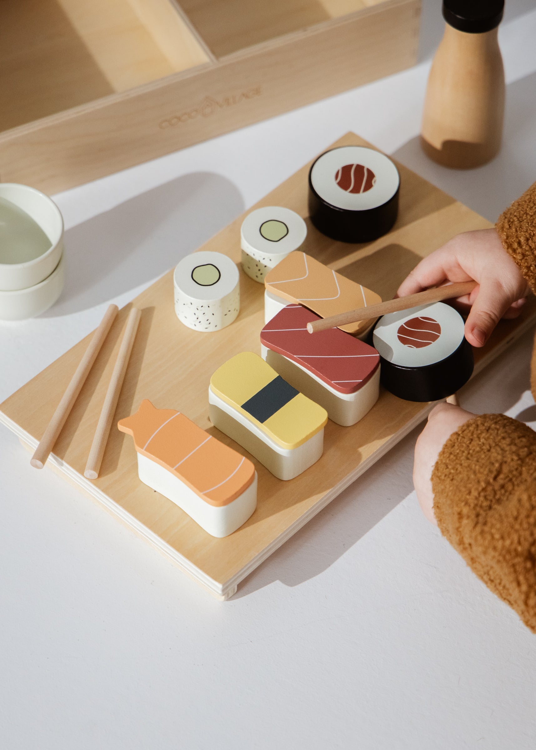 Wooden toy set of sushi on a wooden board with a hand interacting with it.