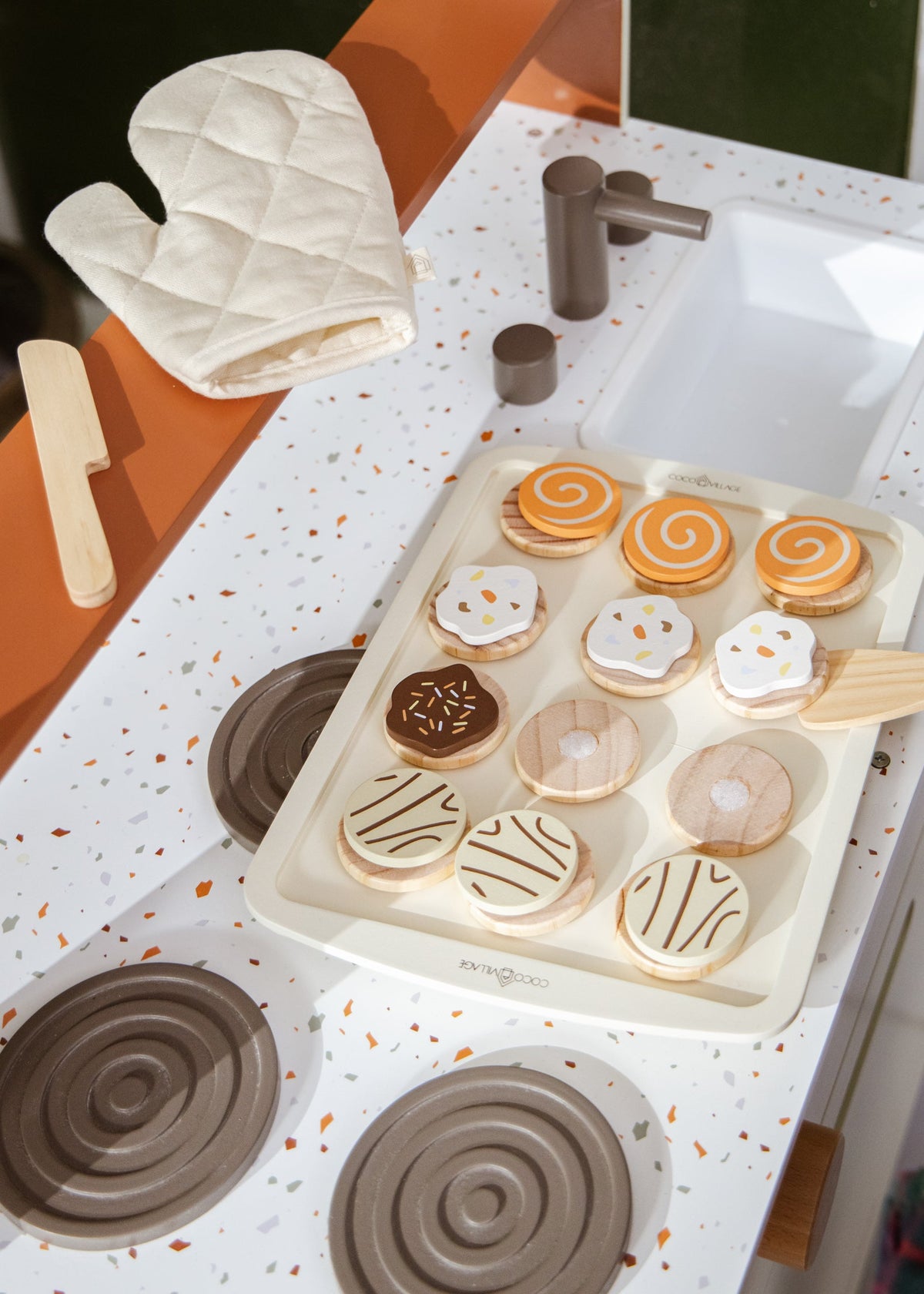 Play kitchen set with baking tray, cookies, and oven mitt on a countertop.