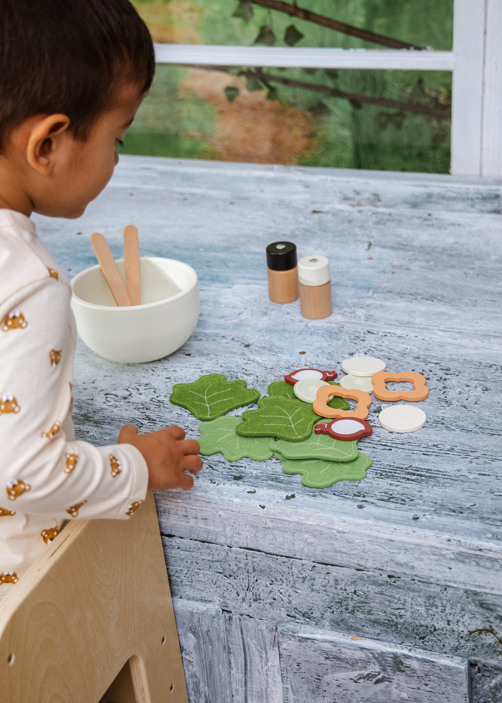 Child playing with green leaf-shaped play dough on a wooden table.