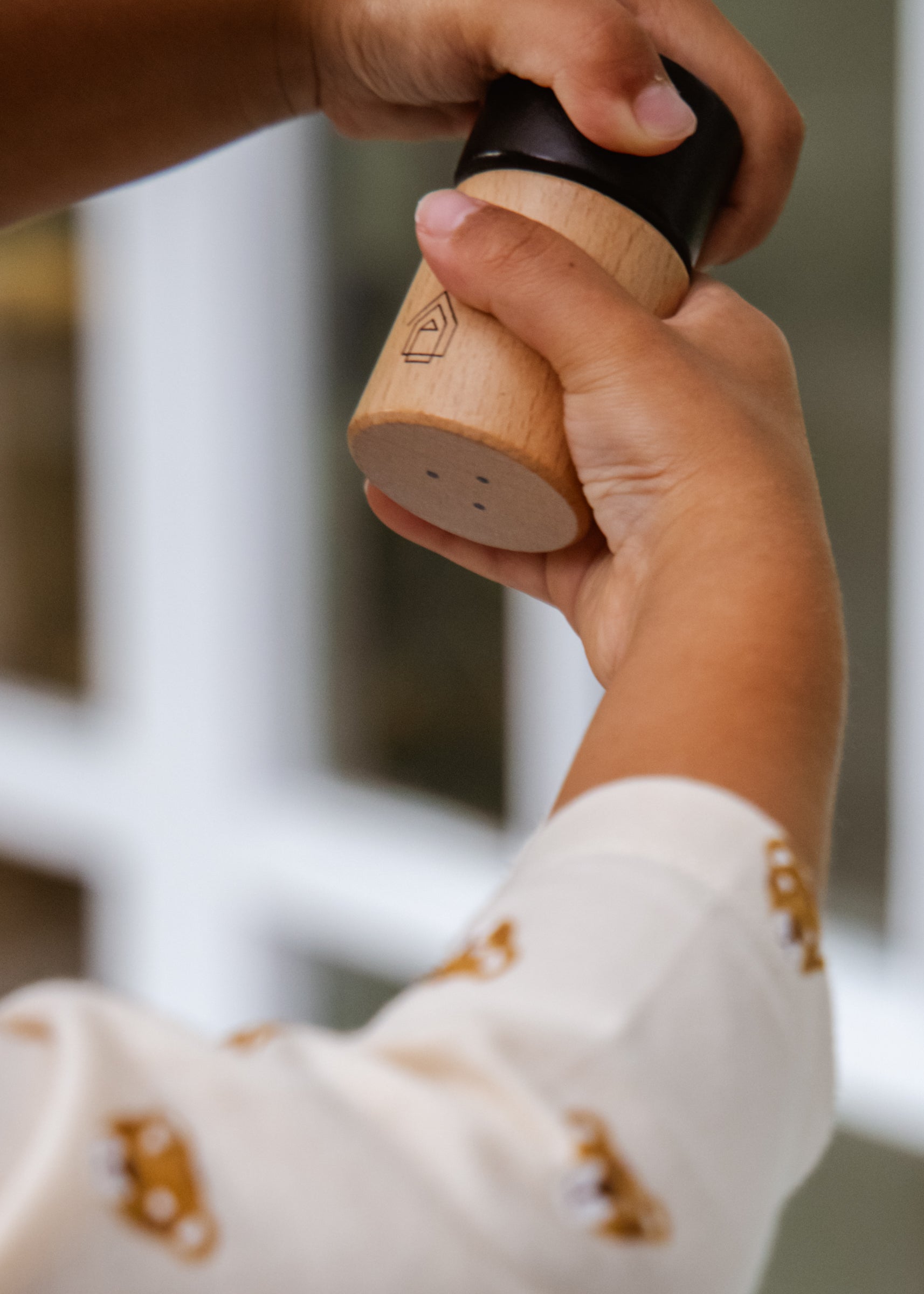 Hand holding a wooden pepper grinder with a blurred background