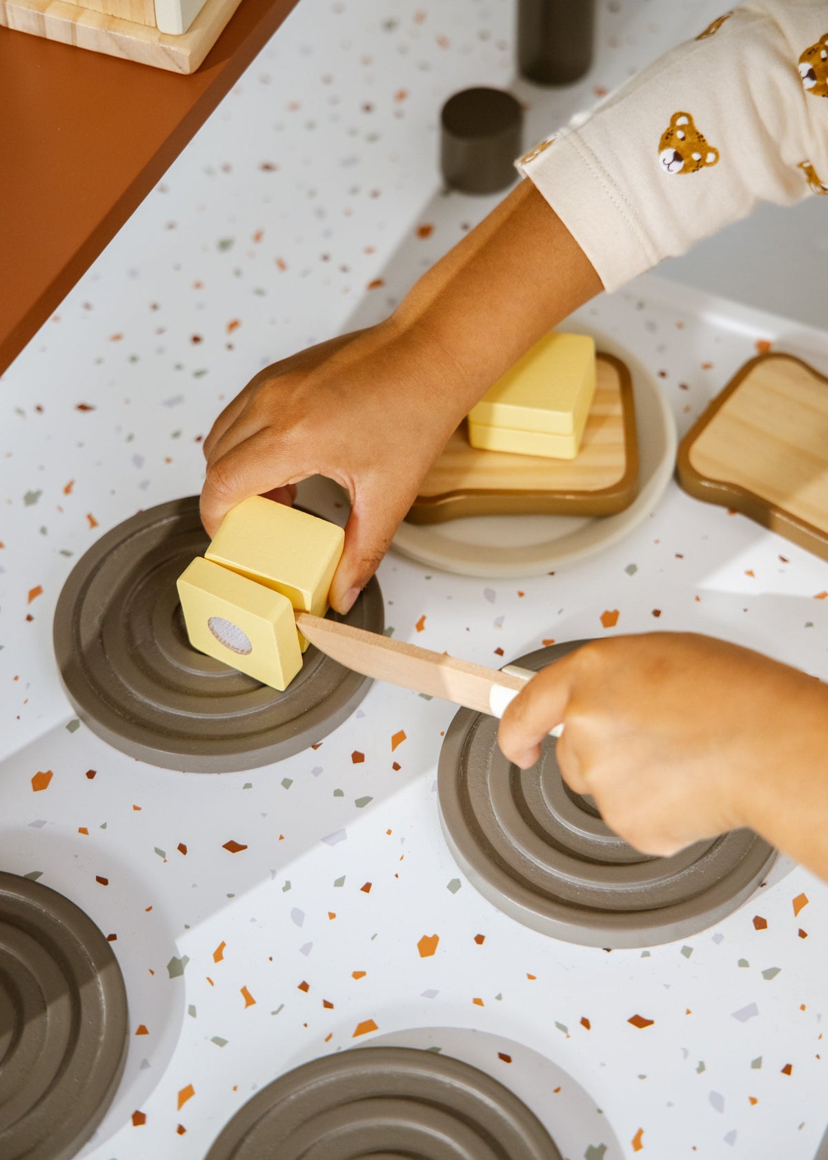 Person using a wooden butter knife to spread butter on bread with a speckled countertop.