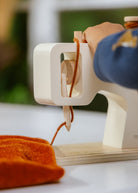 Sewing machine with orange fabric and a hand threading it, blurred background
