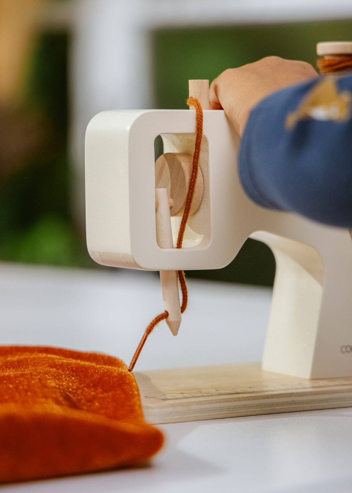 Sewing machine with orange fabric and a hand threading it, blurred background