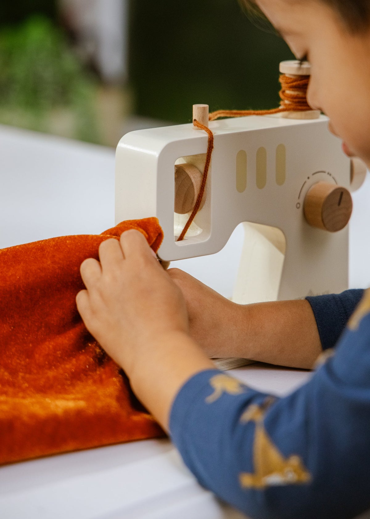 Person using a small white sewing machine on orange fabric.