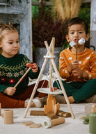 Two children playing with wooden toys including a teepee and campfire.