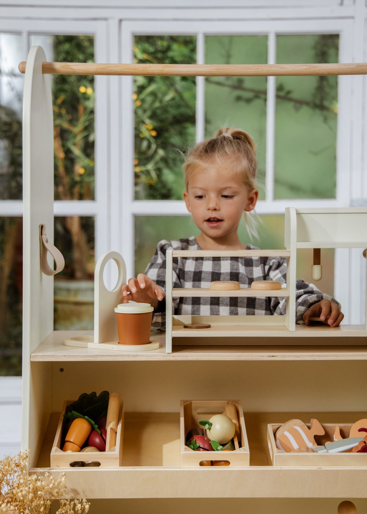 Child playing with a wooden toy kitchen set in a bright room.