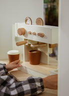 Wooden toy espresso machine with two cups and a person's hand interacting with it.