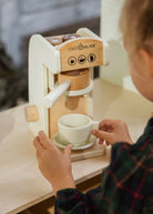 Child playing with a wooden coffee maker toy on a table.