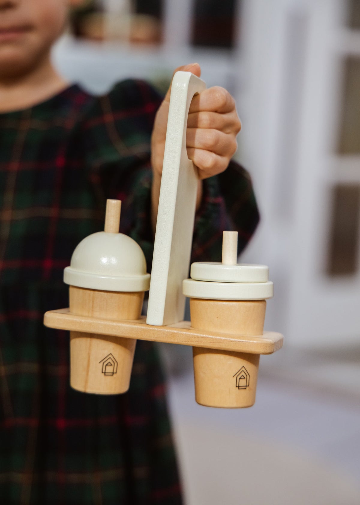 Child holding a wooden toy with two cups and a handle